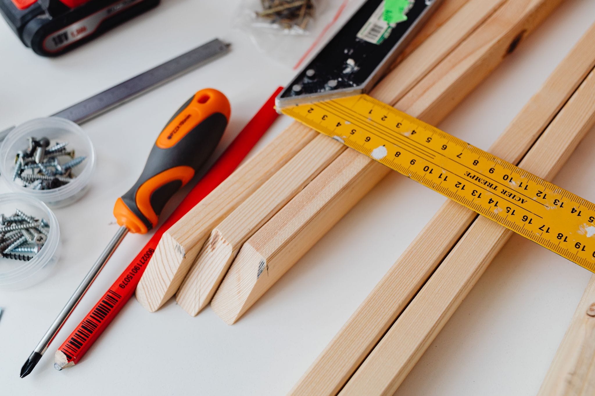 Carpenter's pencil, square, and screws piled on wood planks